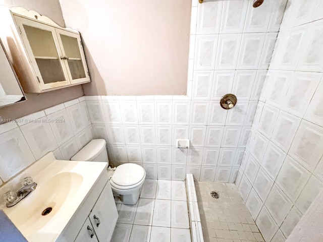 bathroom with a tile shower, tile patterned floors, toilet, vanity, and tile walls