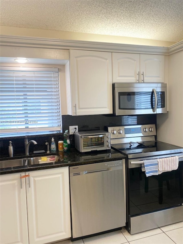 kitchen with appliances with stainless steel finishes, a textured ceiling, sink, white cabinetry, and light tile patterned flooring