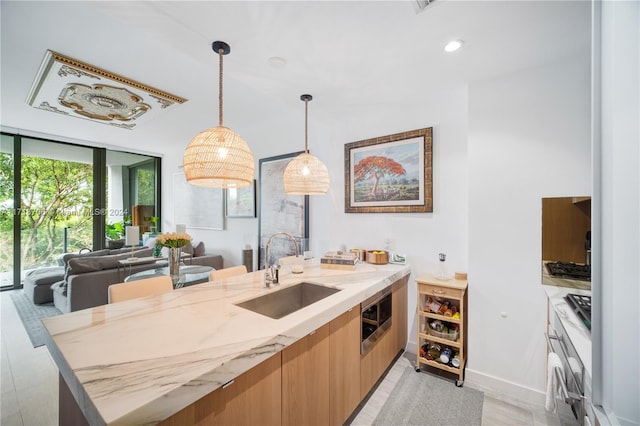 kitchen with stainless steel microwave, light stone counters, sink, and pendant lighting