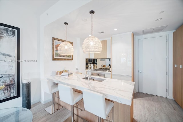 kitchen featuring kitchen peninsula, light stone countertops, sink, pendant lighting, and light hardwood / wood-style flooring