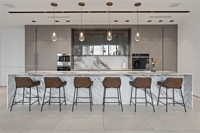 kitchen with a breakfast bar area, gray cabinetry, backsplash, and hanging light fixtures