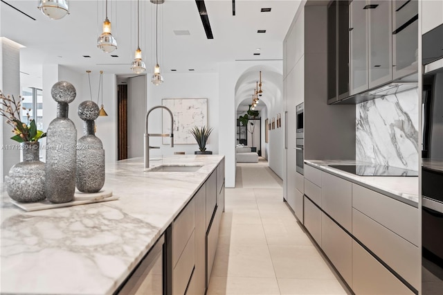 kitchen featuring black electric stovetop, sink, hanging light fixtures, gray cabinets, and light stone counters