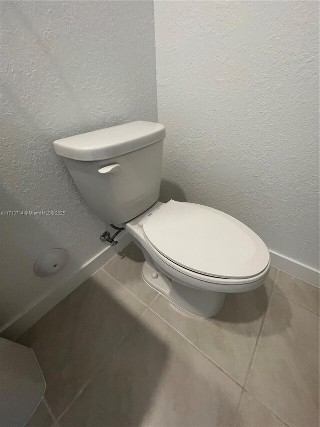 495 NE 5th Ln, Florida City, FL 33034 - bathroom featuring tile patterned flooring, a textured wall, toilet, and baseboards