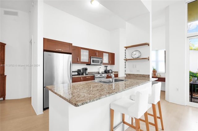 kitchen featuring sink, stainless steel appliances, kitchen peninsula, a towering ceiling, and a breakfast bar