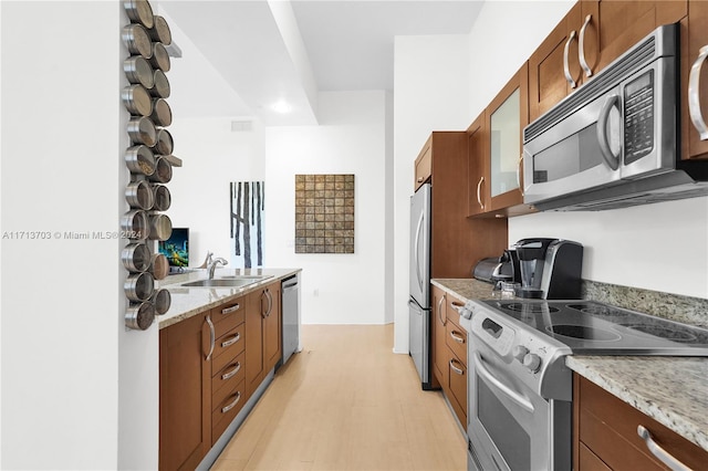 kitchen featuring appliances with stainless steel finishes, light wood-type flooring, light stone counters, and sink