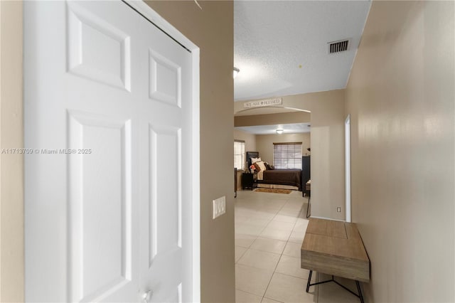 corridor with light tile patterned floors, visible vents, arched walkways, and a textured ceiling