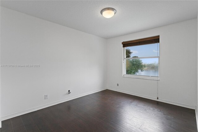 empty room featuring a textured ceiling, an inviting chandelier, and dark wood-type flooring