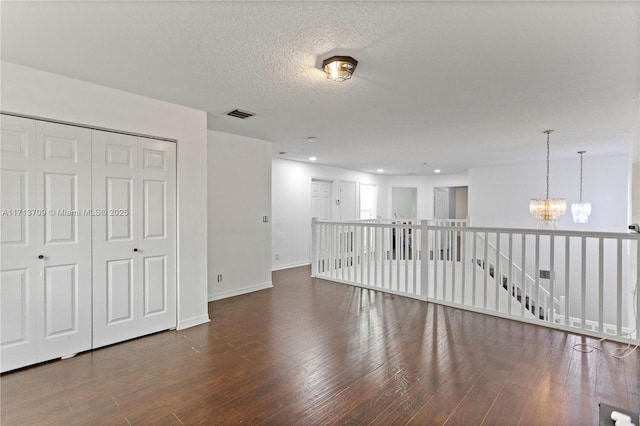 unfurnished room featuring visible vents, a notable chandelier, a textured ceiling, wood finished floors, and baseboards