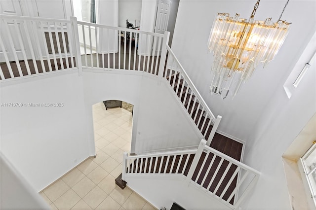 stairway featuring tile patterned flooring, a notable chandelier, and a towering ceiling