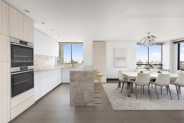 kitchen featuring sink, a kitchen island, white cabinets, stainless steel double oven, and backsplash