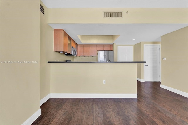 kitchen with dark hardwood / wood-style flooring, kitchen peninsula, stainless steel appliances, and a tray ceiling