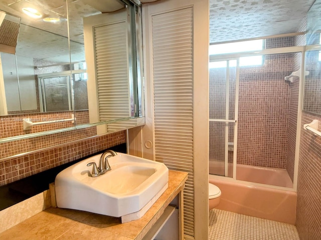 full bathroom with bath / shower combo with glass door, sink, tile patterned floors, and toilet