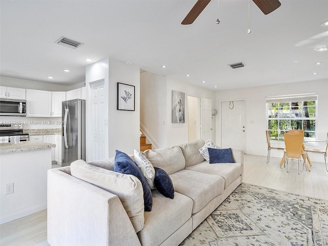 living room featuring visible vents, a ceiling fan, light wood-style floors, and stairs