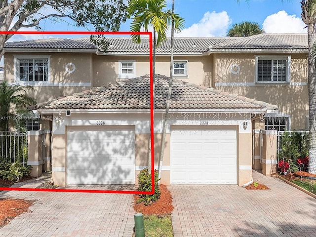 view of front of home featuring a tiled roof, fence, decorative driveway, and stucco siding
