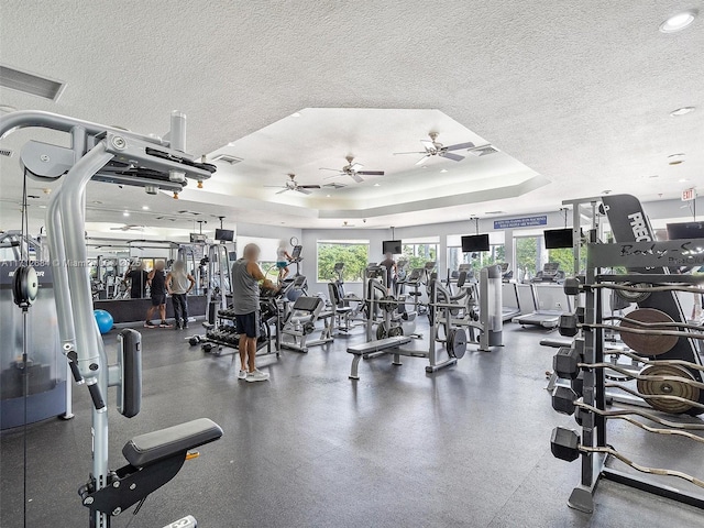workout area with a raised ceiling, a textured ceiling, a ceiling fan, and visible vents