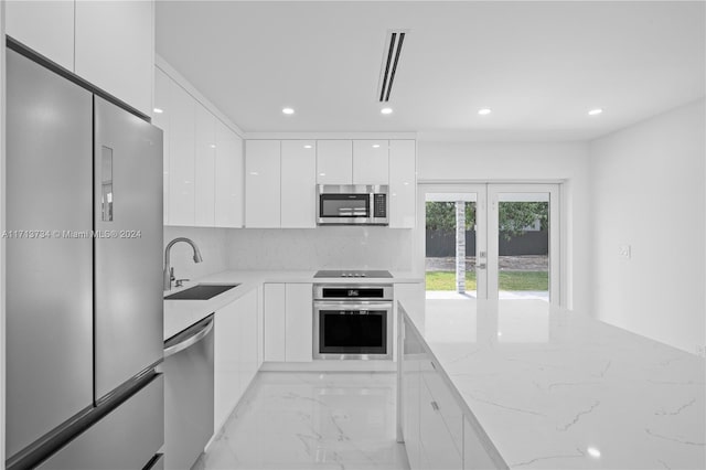 kitchen with sink, white cabinetry, light stone counters, stainless steel appliances, and decorative backsplash