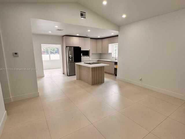 kitchen with stainless steel fridge, vaulted ceiling, sink, light tile patterned floors, and a center island