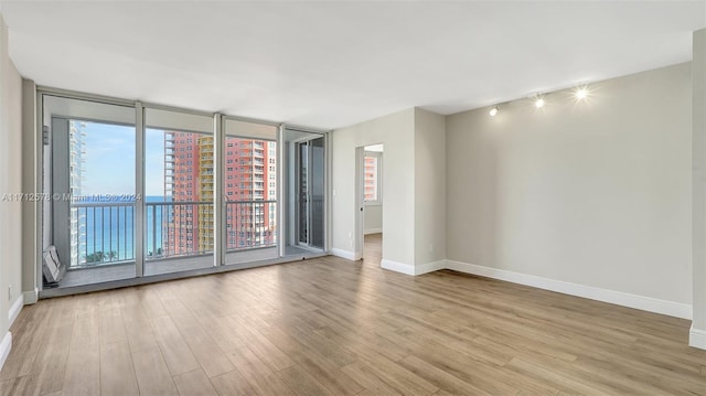 spare room with light wood-type flooring, a water view, and floor to ceiling windows