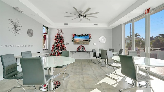 dining area with a raised ceiling, ceiling fan, and light tile patterned floors