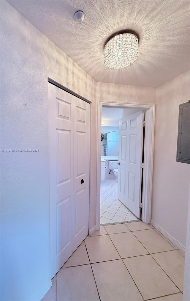 corridor with a notable chandelier, light tile patterned floors, and electric panel