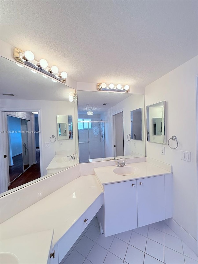 bathroom with a textured ceiling, vanity, tile patterned floors, and a shower with door