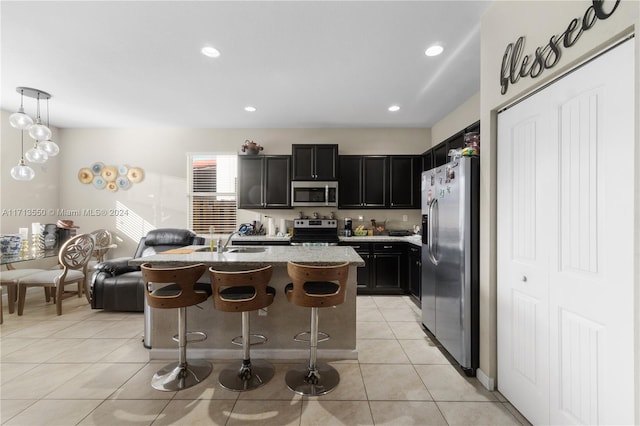 kitchen featuring stainless steel appliances, decorative light fixtures, a breakfast bar area, a center island with sink, and light tile patterned floors