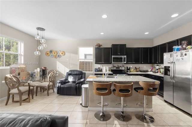 kitchen featuring light stone countertops, stainless steel appliances, a kitchen island with sink, decorative light fixtures, and light tile patterned flooring