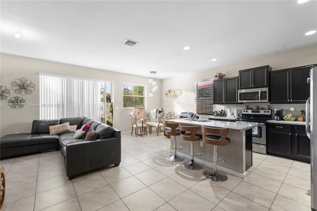 kitchen featuring light stone countertops, a kitchen breakfast bar, stainless steel appliances, pendant lighting, and a center island with sink