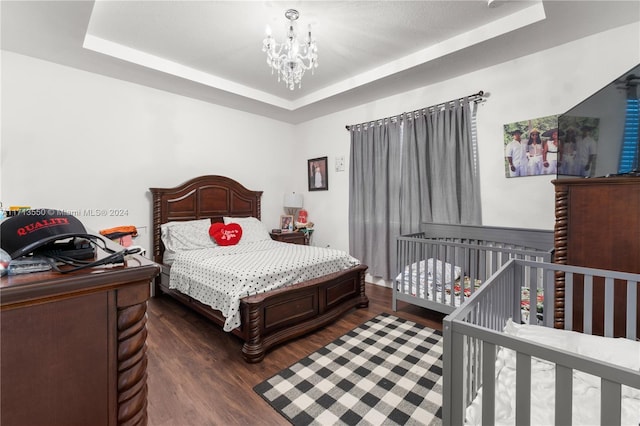 bedroom featuring a chandelier, a raised ceiling, and dark wood-type flooring