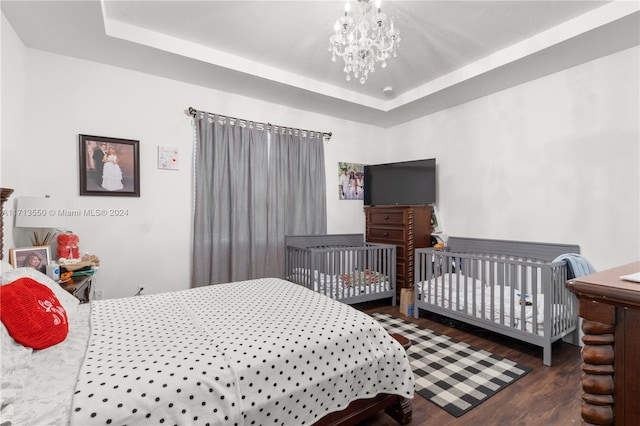 bedroom with dark hardwood / wood-style floors, an inviting chandelier, a raised ceiling, and a nursery area