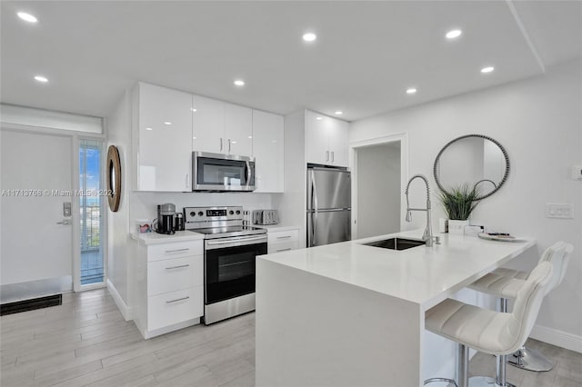 kitchen with sink, stainless steel appliances, kitchen peninsula, a breakfast bar area, and white cabinets