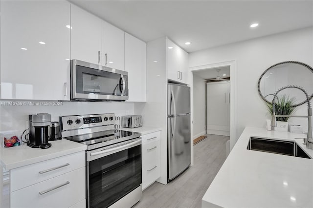 kitchen with stainless steel appliances, white cabinetry, light hardwood / wood-style floors, and sink