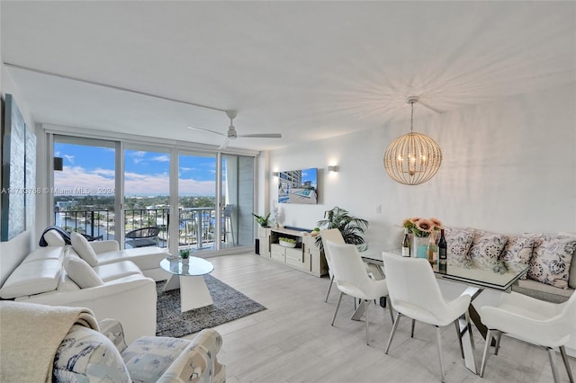 living room featuring light hardwood / wood-style flooring, ceiling fan with notable chandelier, and a wall of windows