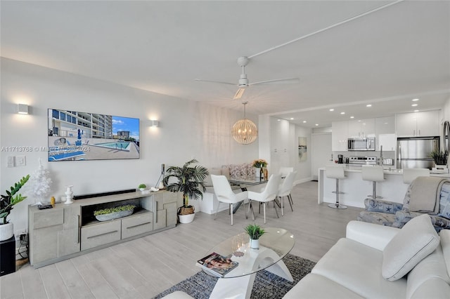 living room featuring light wood-type flooring and ceiling fan with notable chandelier