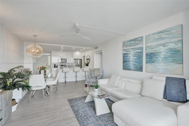 living room featuring ceiling fan with notable chandelier and light hardwood / wood-style flooring