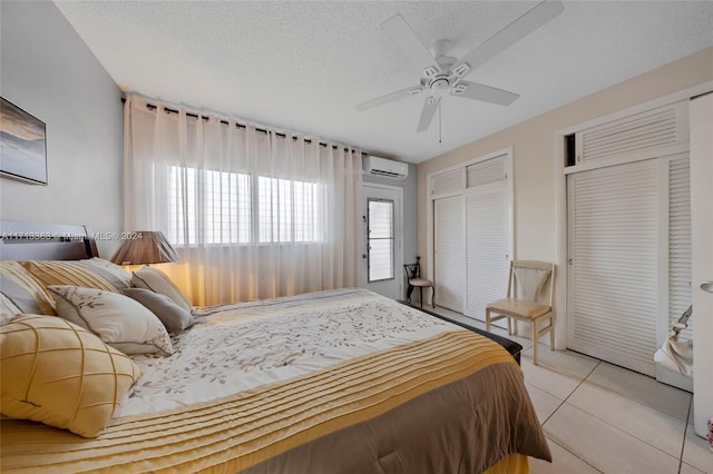 tiled bedroom with a textured ceiling, two closets, an AC wall unit, and ceiling fan