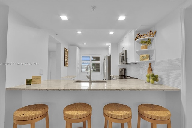 kitchen featuring kitchen peninsula, appliances with stainless steel finishes, decorative backsplash, sink, and white cabinets