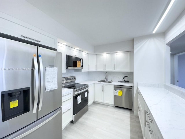 kitchen featuring white cabinets, sink, decorative backsplash, light stone countertops, and stainless steel appliances