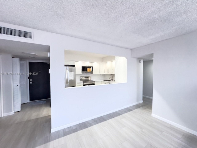 unfurnished living room with light wood-type flooring and a textured ceiling