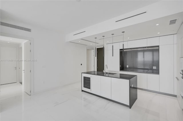 kitchen with pendant lighting, a center island with sink, white cabinetry, and sink