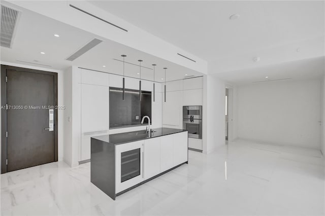 kitchen with a kitchen island with sink, white cabinetry, sink, and hanging light fixtures