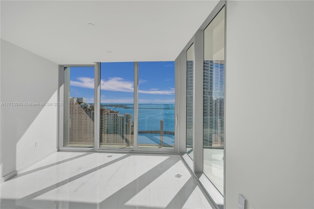 empty room with floor to ceiling windows, a water view, and light tile patterned floors