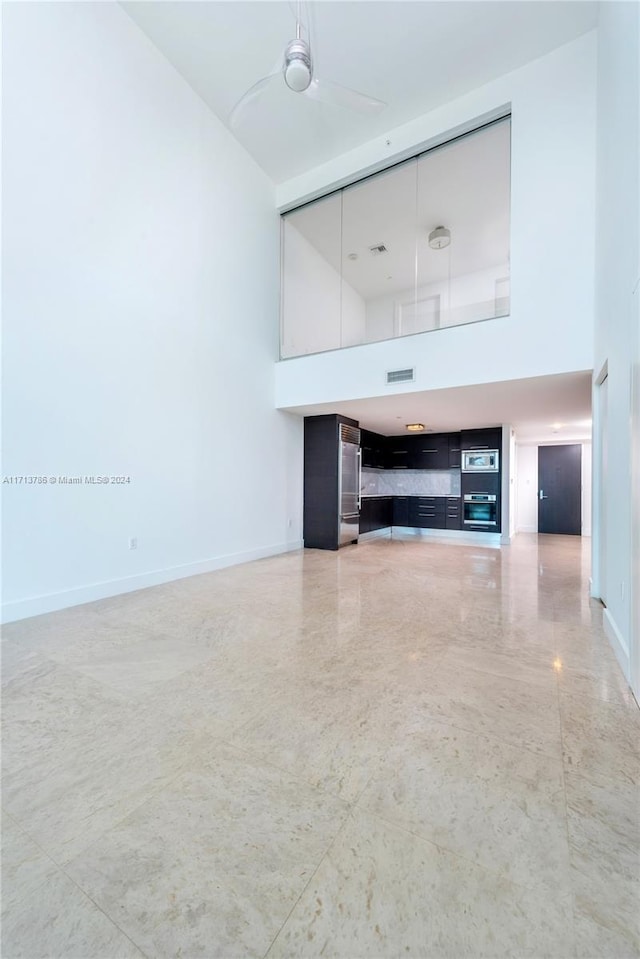 unfurnished living room featuring ceiling fan and a high ceiling