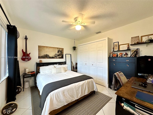 bedroom with ceiling fan, a closet, light tile patterned floors, and a textured ceiling