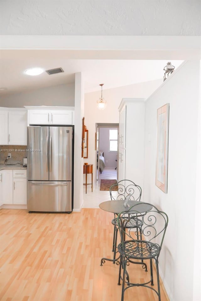 kitchen featuring stainless steel fridge, backsplash, vaulted ceiling, white cabinetry, and hanging light fixtures