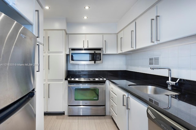 kitchen featuring decorative backsplash, stainless steel appliances, sink, dark stone countertops, and white cabinetry