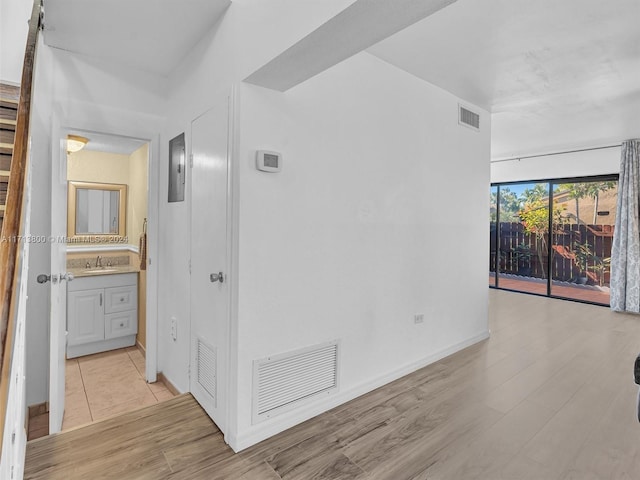 hall with electric panel, sink, and light wood-type flooring