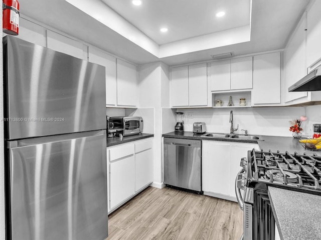 kitchen with stainless steel appliances, a raised ceiling, sink, white cabinets, and light hardwood / wood-style floors