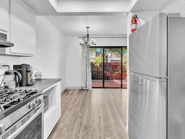 kitchen with appliances with stainless steel finishes, light wood-type flooring, pendant lighting, an inviting chandelier, and white cabinets