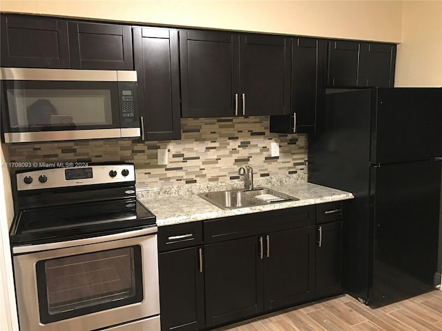 kitchen with appliances with stainless steel finishes, backsplash, light stone counters, sink, and light hardwood / wood-style flooring